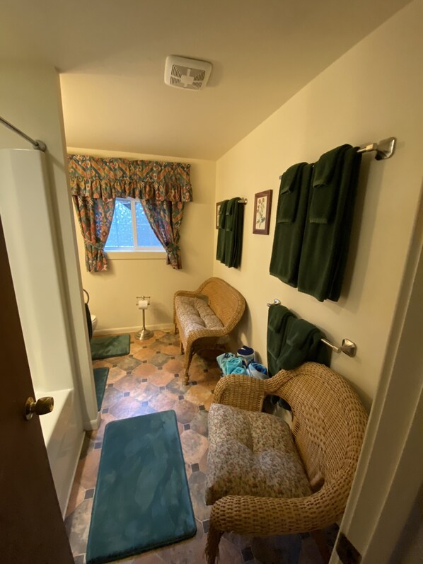 Una habitación pequeña y acogedora con una silla de mimbre, un banco y una ventana con cortinas estampadas.