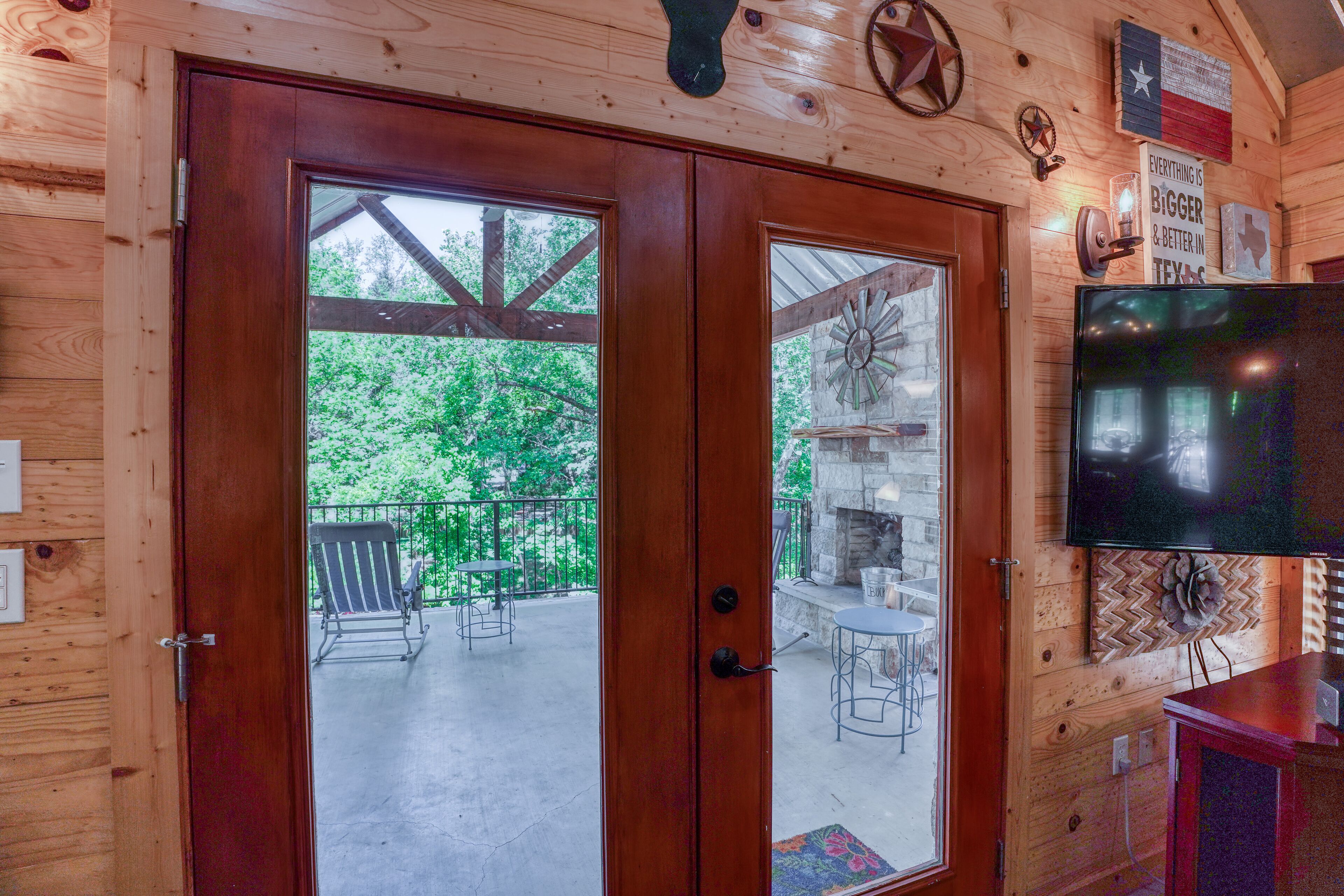 A wooden cabin with a large glass door leading to an outdoor patio with a barbecue area and seating.