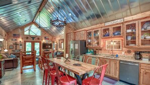 Una cocina amplia con armarios de madera, un comedor con mesa de madera y sillas rojas, y un techo alto con vigas metálicas.