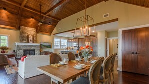A spacious living area with a fireplace, dining table set for six, and a kitchen in the background.