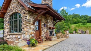 A stone house with a wooden porch, a fireplace, and a garden with flowers and plants.