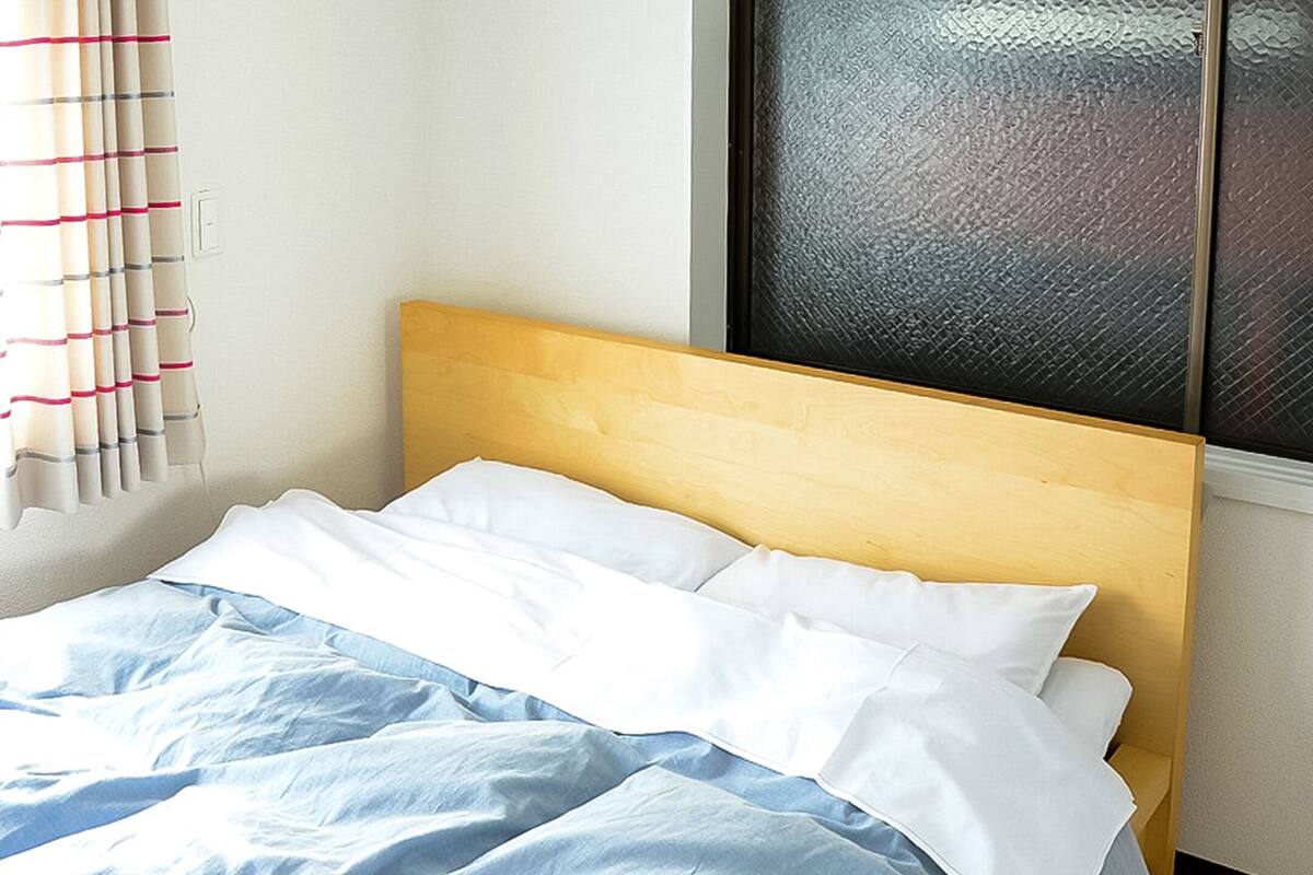 A neatly made bed with white and blue bedding, a wooden headboard, and a window with a textured glass view.