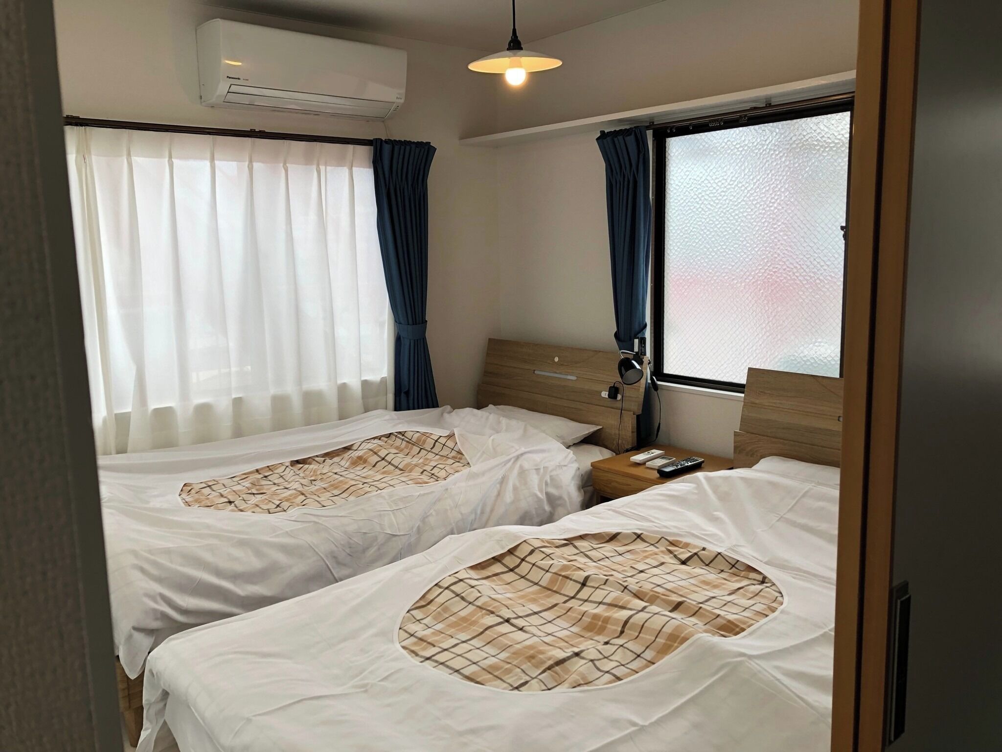 Ein Hotelzimmer mit zwei Betten, einem Holzkopfstück, einem Nachttisch mit Lampe und einer Klimaanlage an der Wand.