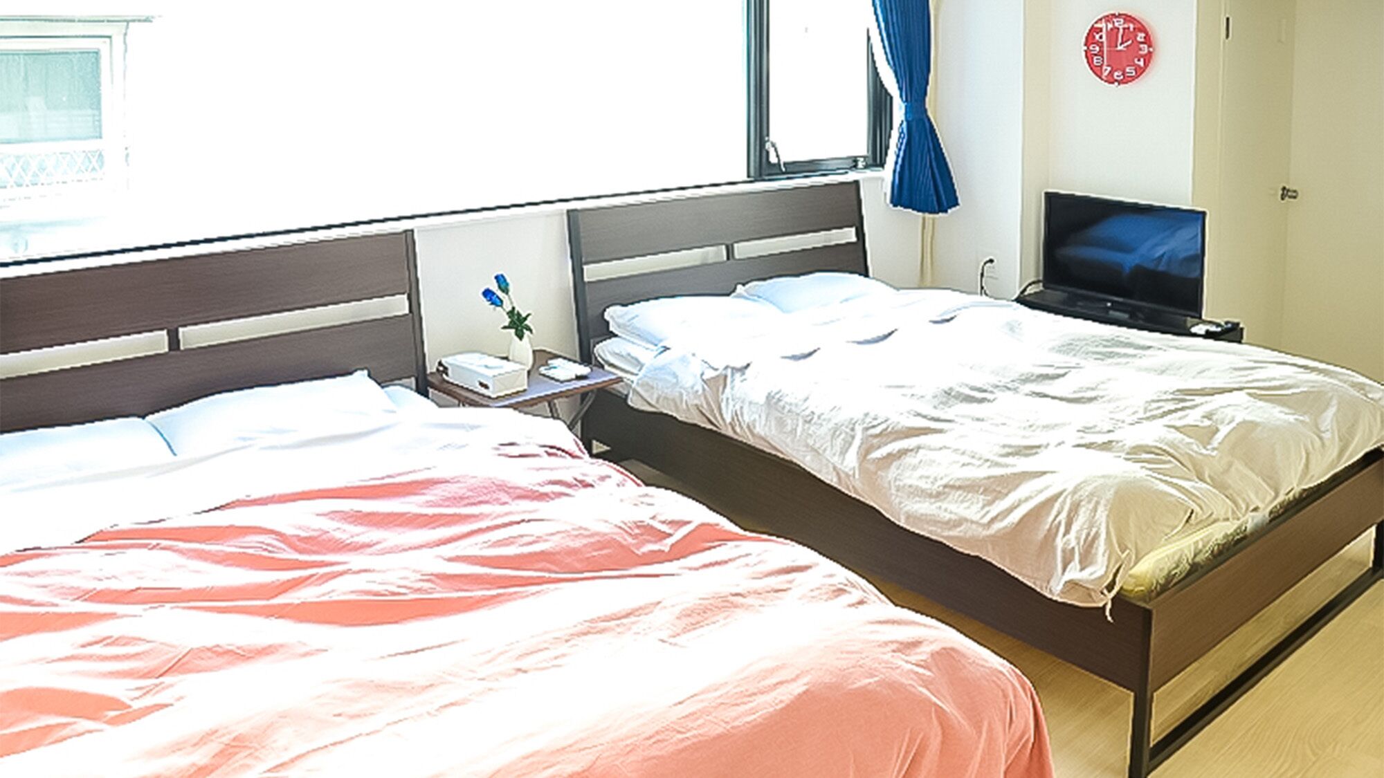 Een hotelkamer met twee bedden, een televisie, een klok en een raam met gordijnen.