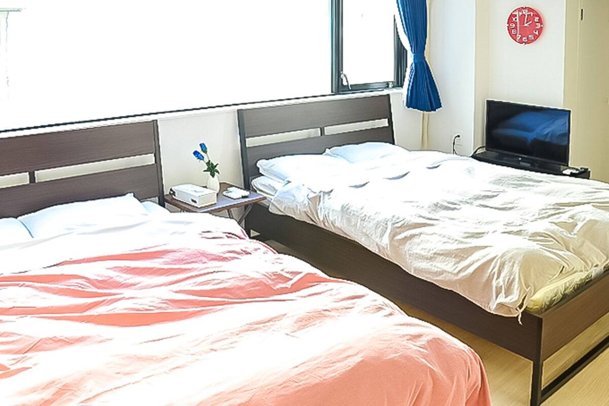 A hotel room with two beds, a TV, a clock, and a window with curtains.