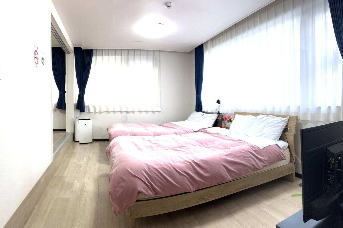 A bedroom with a wooden bed, white walls, and a large window with curtains.
