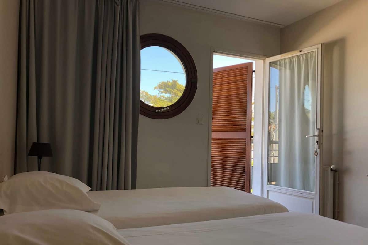 A bedroom with two beds, a window with a view of trees, and a door leading outside.