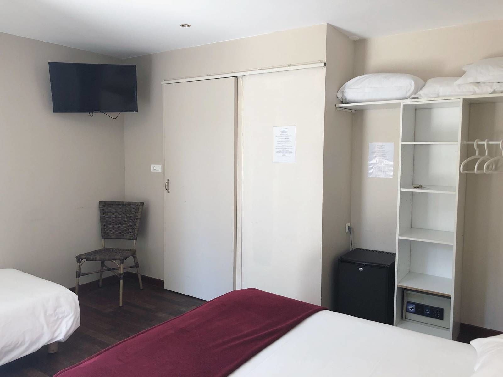 A hotel room with a bed, a chair, a wardrobe, a television, and a small black appliance.