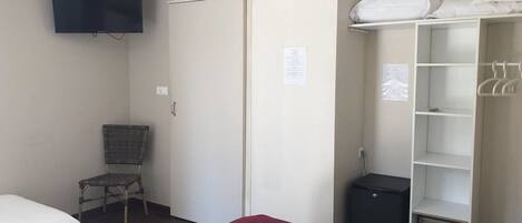 A hotel room with a bed, a chair, a wardrobe, a television, and a small black appliance.