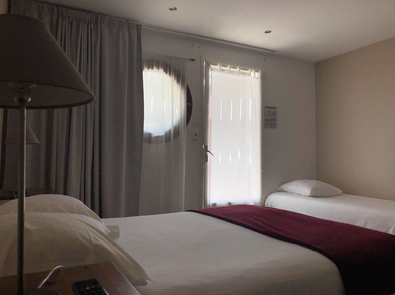 Habitación de hotel con cama, escritorio, lámpara y ventana con cortinas.