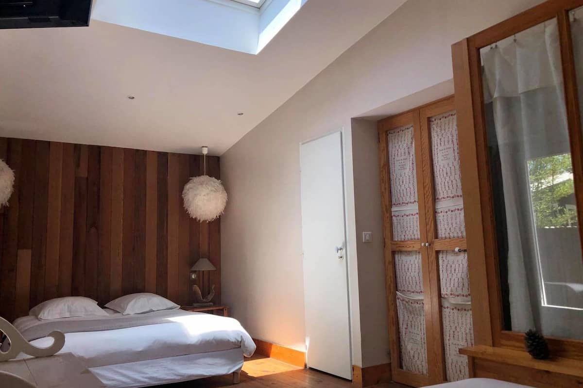 A bedroom with two beds, wooden panel walls, a skylight, and a large window with curtains.