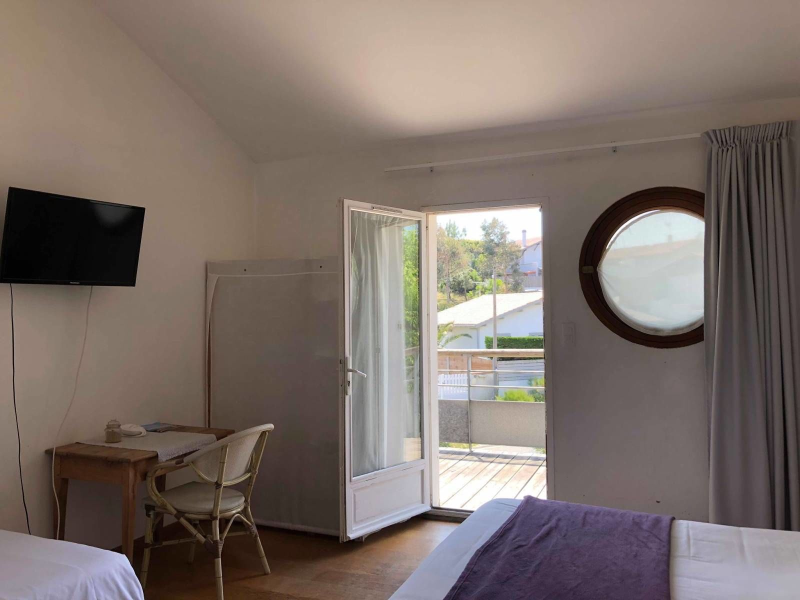 A bedroom with a bed, a desk, a chair, a television, a window, and a balcony.