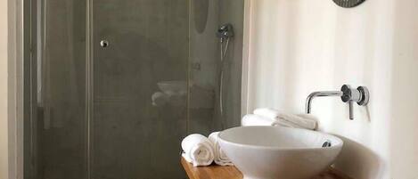 A bathroom with a glass-enclosed shower, a wooden vanity with a white sink, and a round mirror.