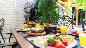 A breakfast table with various food items and drinks, set outdoors with a brick wall and greenery in the background. - Tuzla Garden Hotel & Spa (Tuzla)