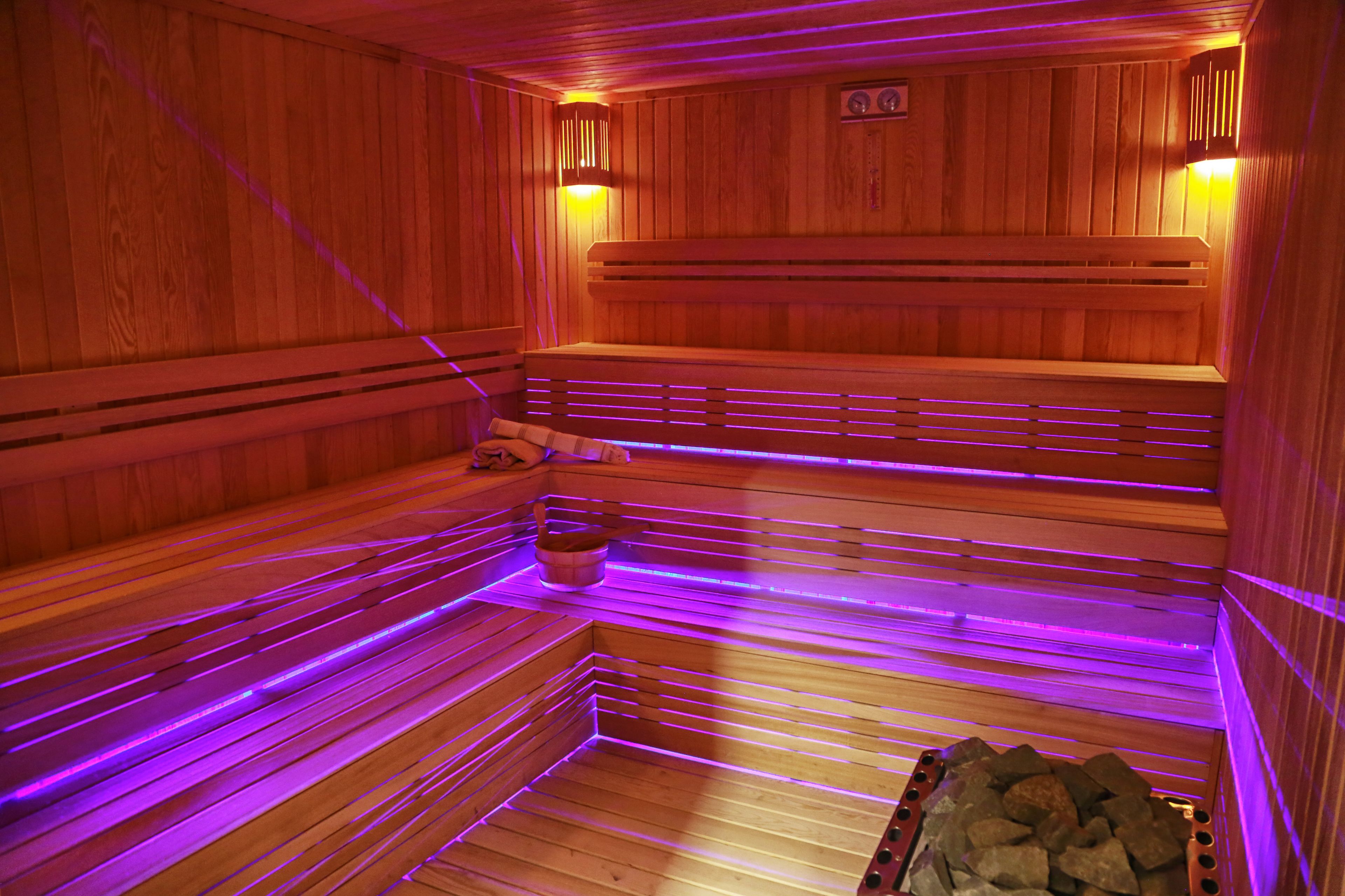 A sauna with wooden benches, a bucket, and a pile of stones.
