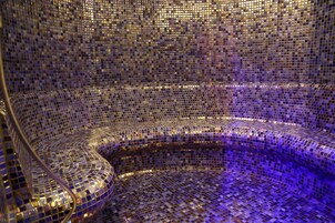 Una habitación con una pared de curvas y un diseño en mosaico, y un suelo reflectante.