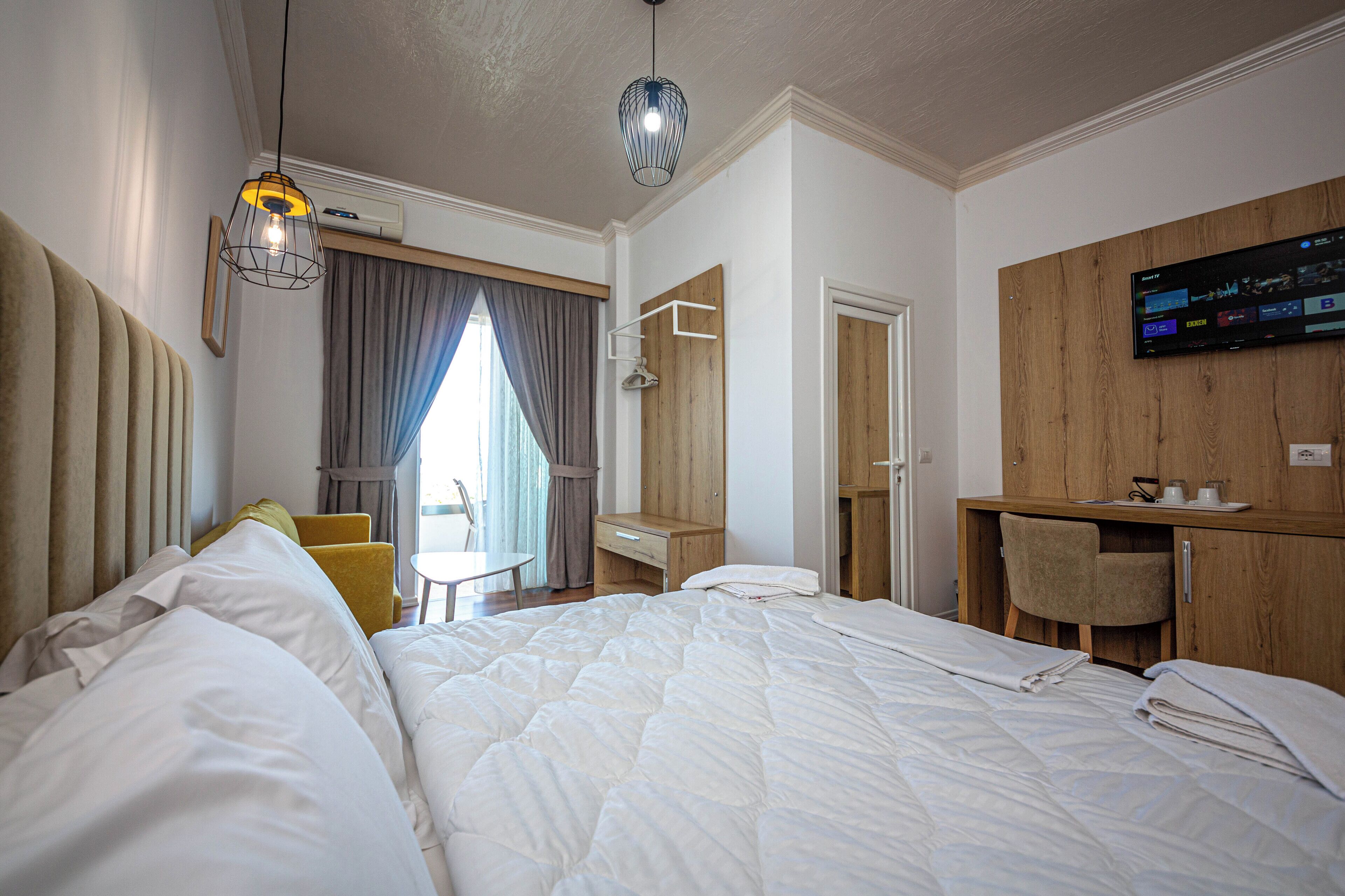 A hotel room with a large bed, a desk, a chair, and a TV mounted on the wall.