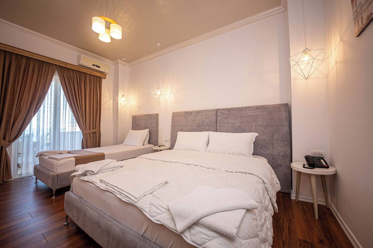 A hotel room with a large bed, a smaller bed, a bedside table with a phone, and a window with curtains.