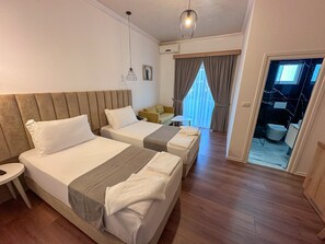 A hotel room with two beds, a small table, a chair, a sofa, and a view of the outside. - Hotel Murati (Ksamil)