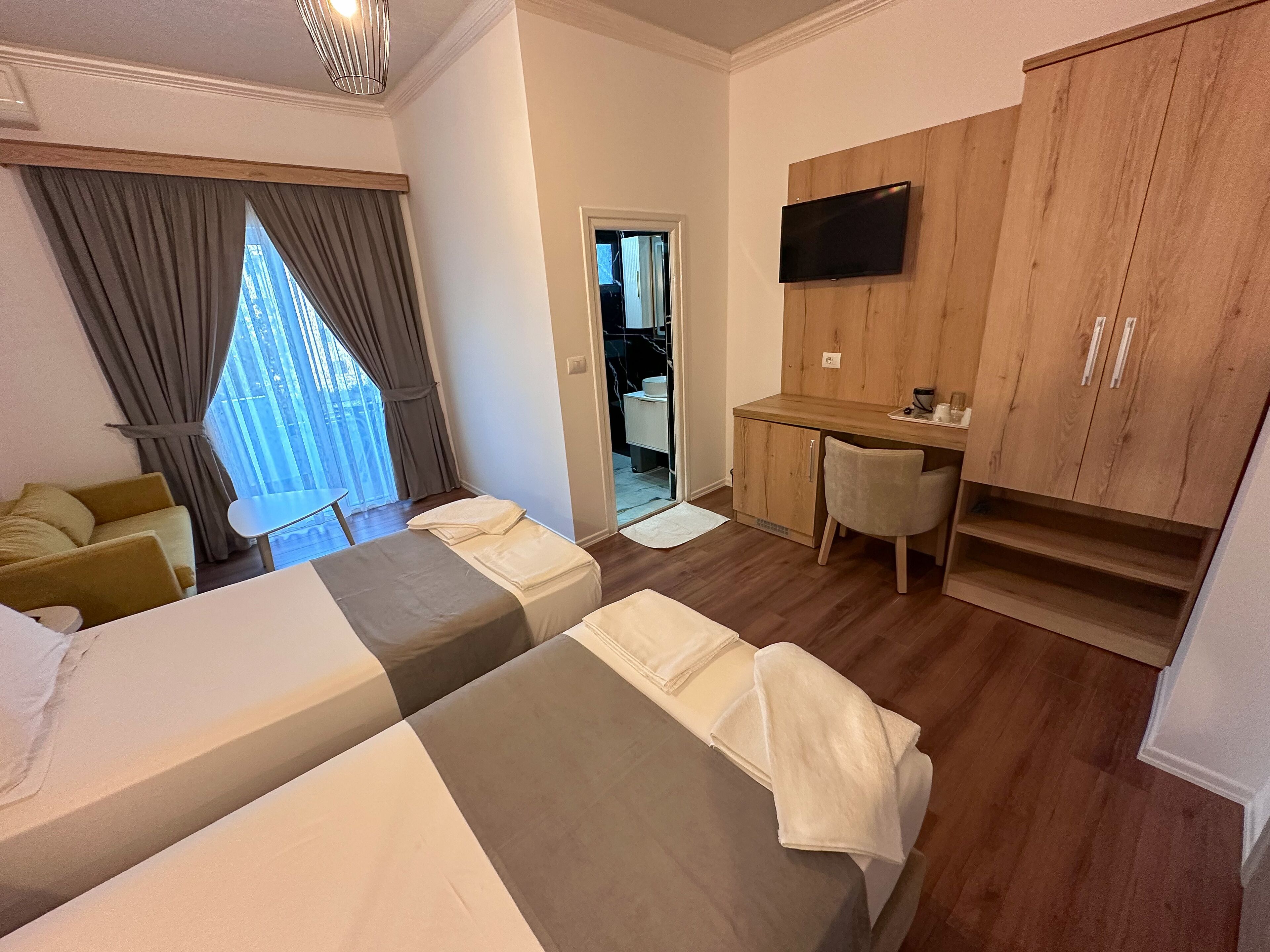 A hotel room with two beds, a desk, a chair, a TV, and a wardrobe.