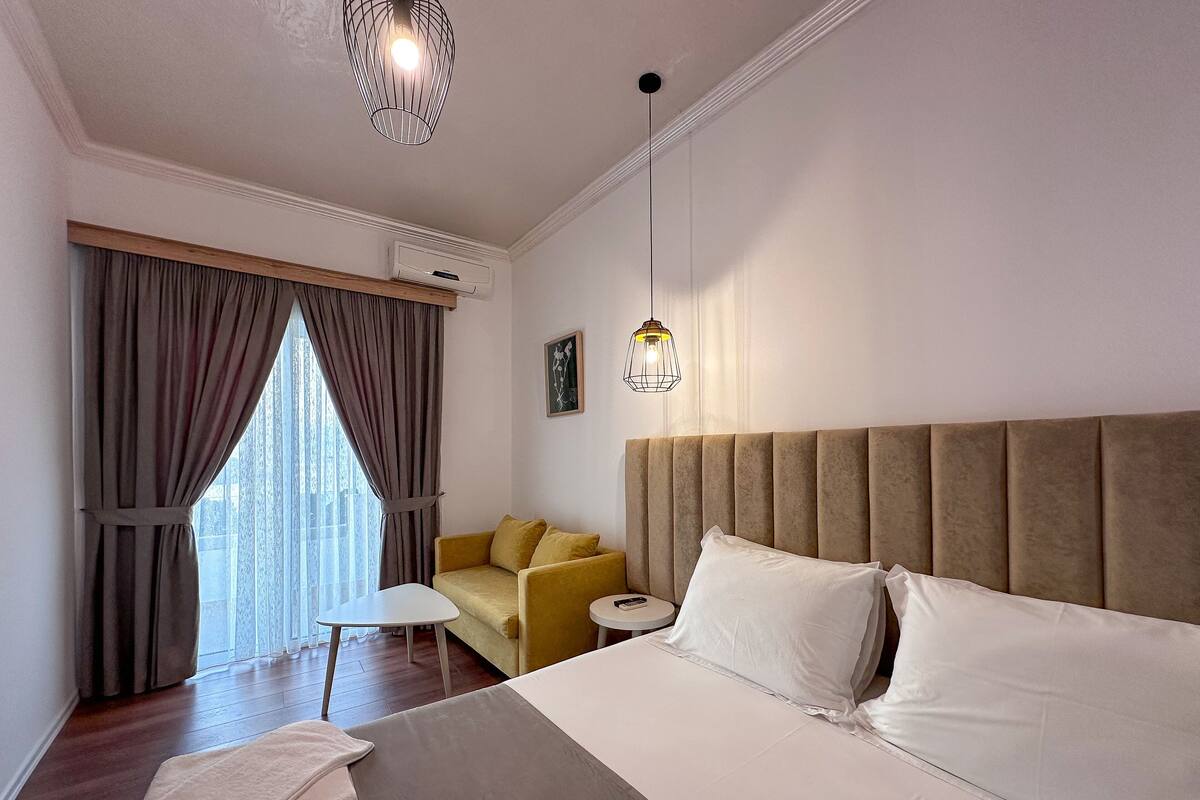 A hotel room with a large bed, a sofa, a small table, and a hanging light fixture.