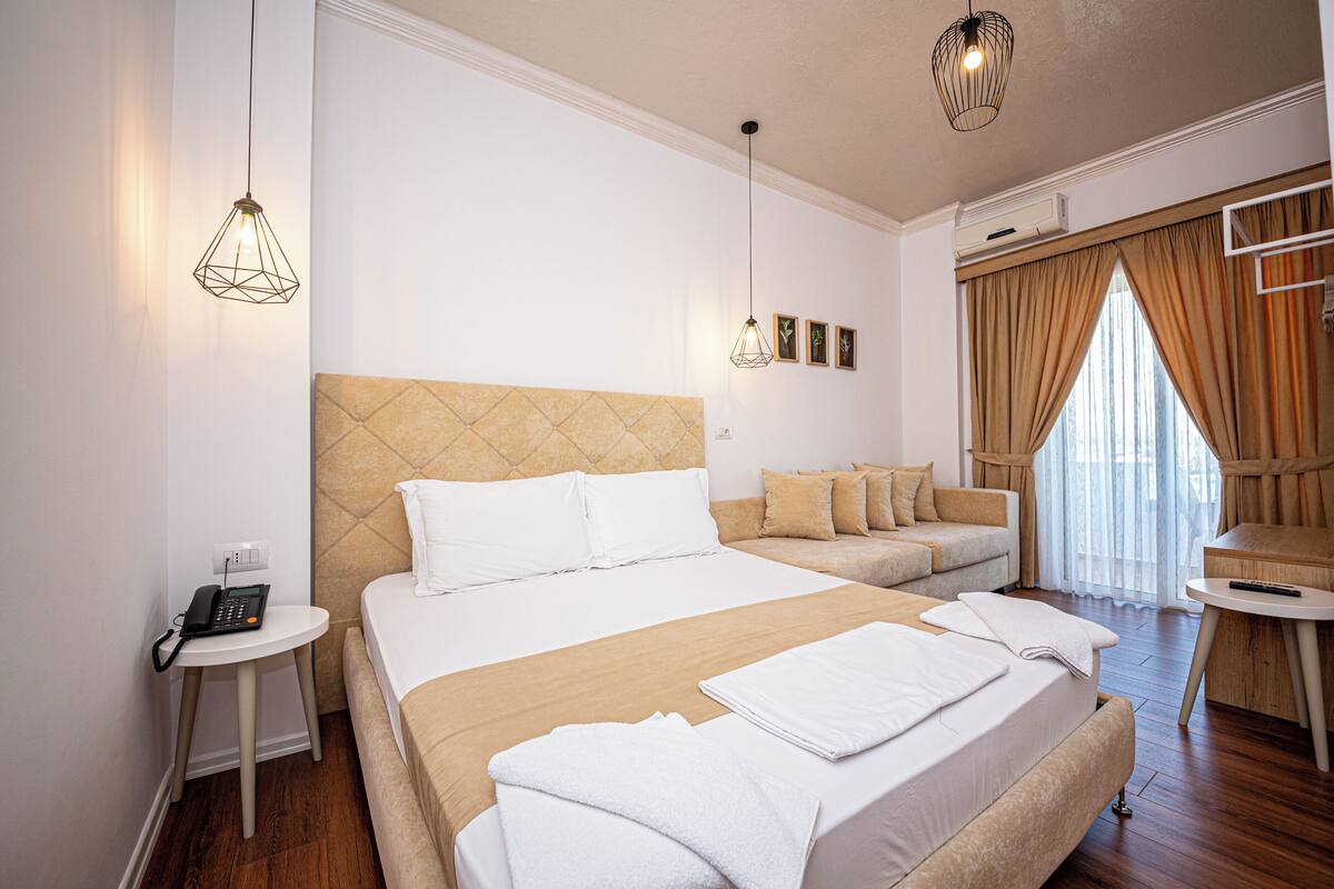 A hotel room with a large bed, a bedside table with a phone, a small round table, and a window with curtains.
