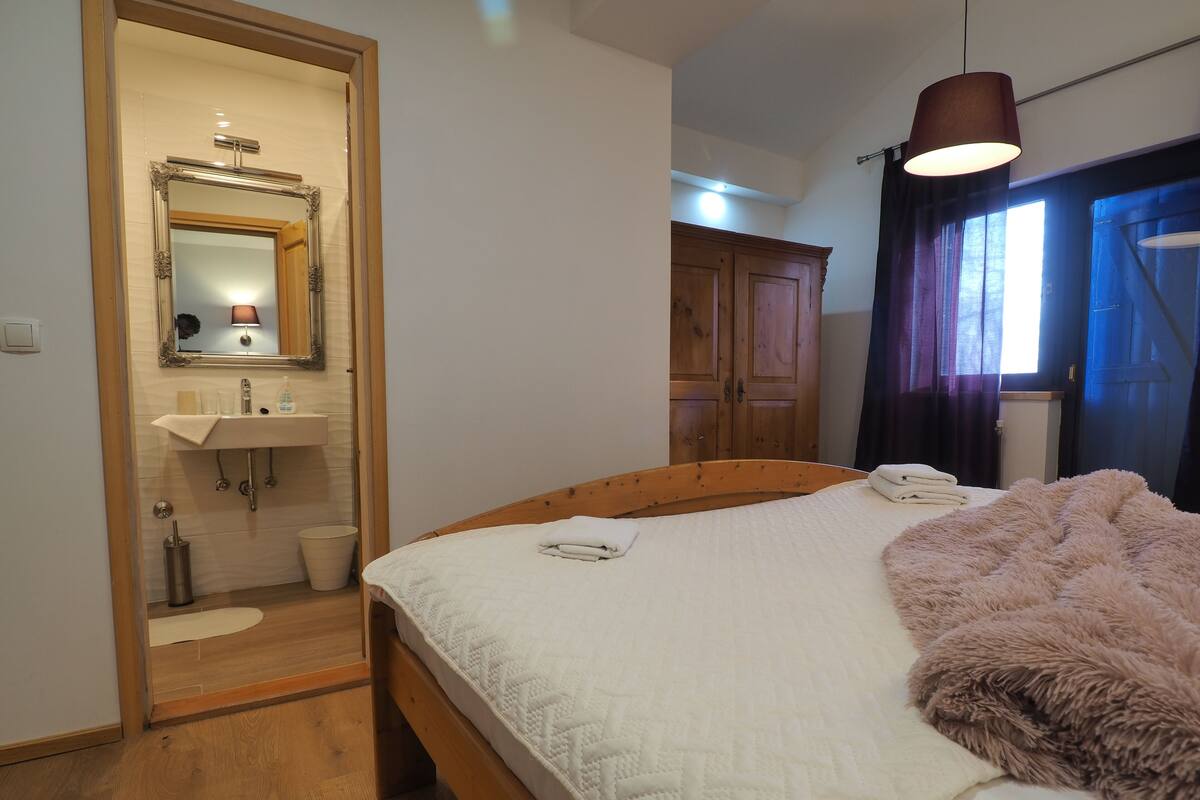 Ein Schlafzimmer mit einem hölzernen Bett, einem Nachttisch, einem Spiegel, einem Waschbecken und einem Kleiderschrank.