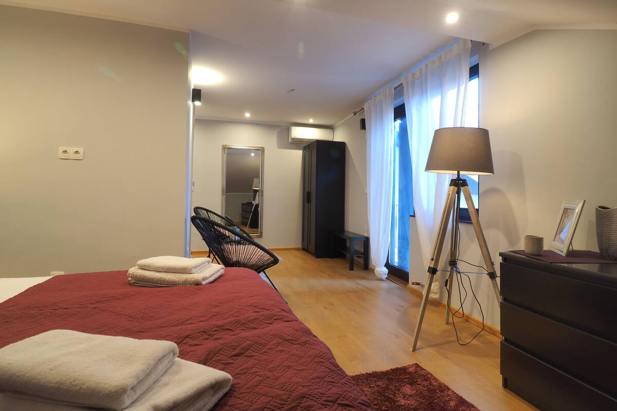 Ein modernes Schlafzimmer mit einem großen Bett, einer Stehlampe, einem Sessel und einer Kommode.
