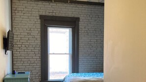 A bedroom with a bed, a green dresser, a gray sofa, a ceiling fan, and a large window.