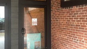 A building entrance with a glass door, a brick wall, and a small window.