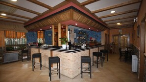 Zona de bar con mostrador de ladrillo, taburetes negros y techo de madera.