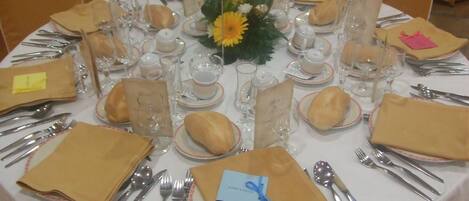 Una mesa redonda dispuesta para una comida formal, con varios puestos que incluyen platos, cubiertos y vasos.