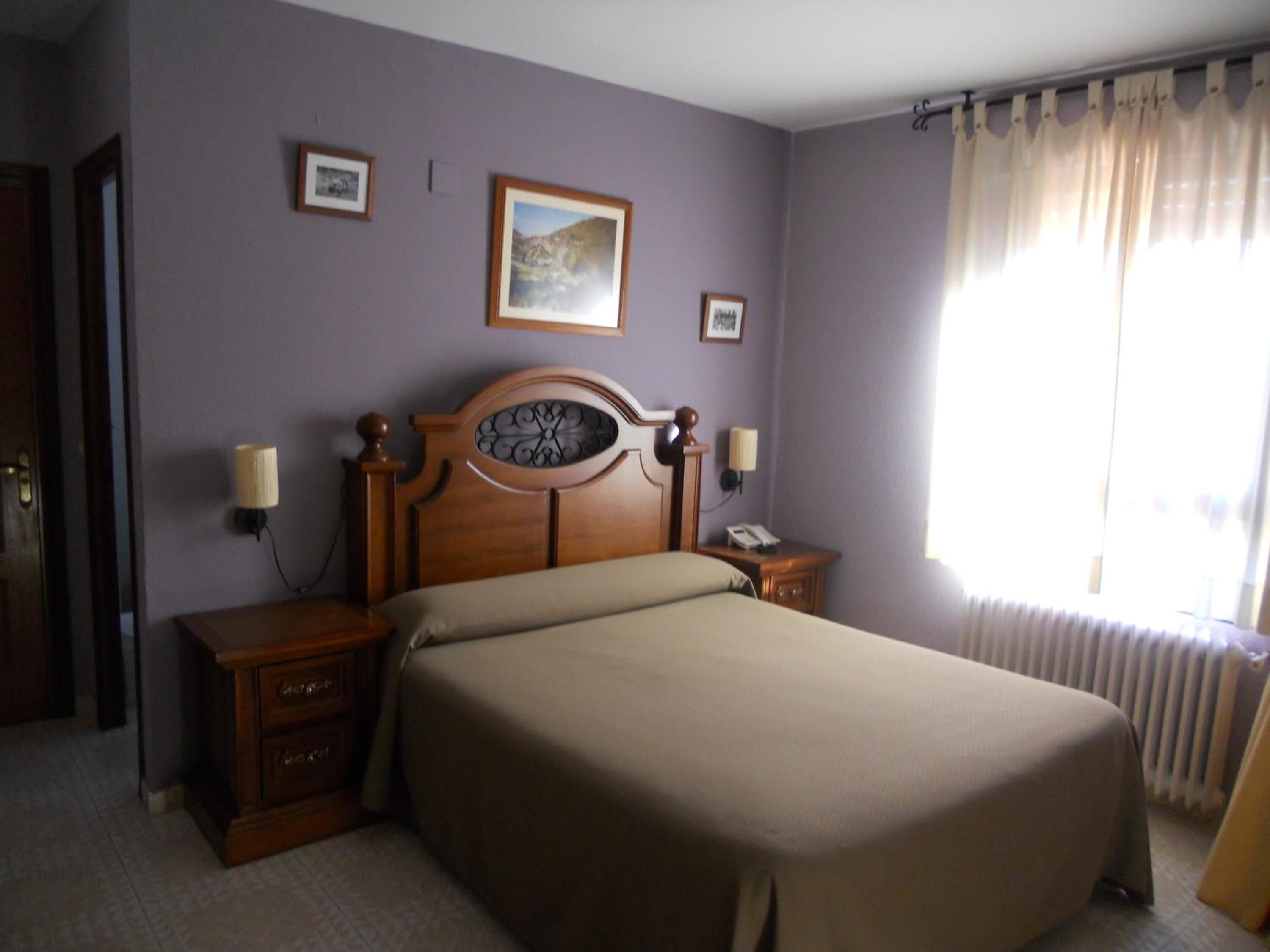 Habitación de hotel con una cama grande, dos mesitas de noche, un teléfono de pared y dos cuadros enmarcados.