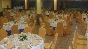 Un salón de banquetes con mesas redondas, cada una cubierta con manteles blancos, sillas doradas y una vajilla elegantemente dispuesta.
