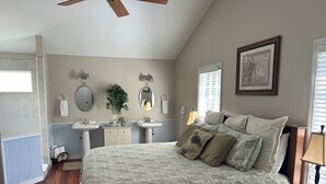 A bedroom with a bed, two bedside tables, a nightstand, a ceiling fan, a window with blinds, a wall-mounted mirror, and a radiator. -  Thomas' Store- Remodeled in Oct 2021, pet friendly (Steinhatchee)