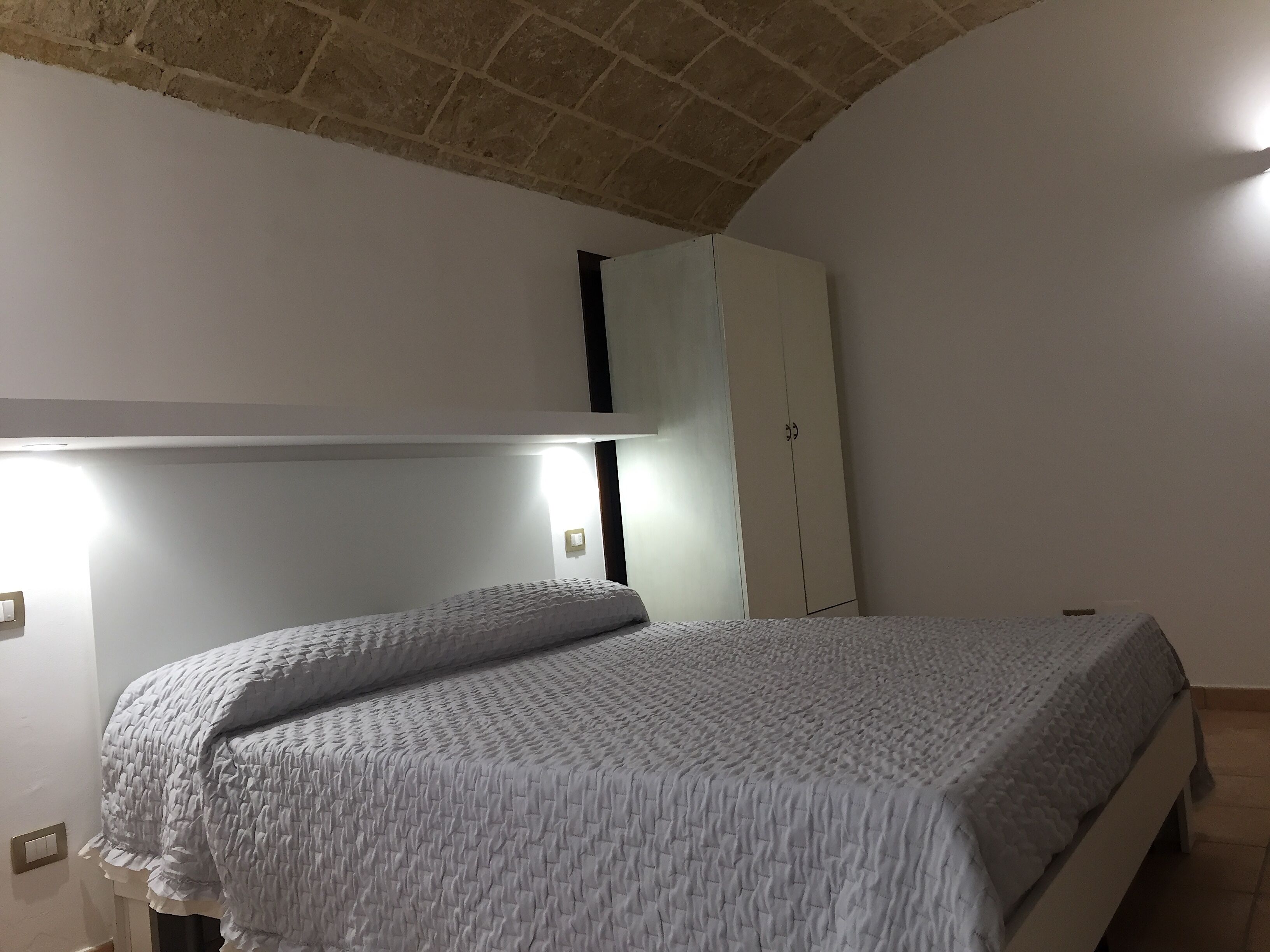 A bedroom with a bed, a wardrobe, and a ceiling with exposed brick.