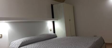 A bedroom with a bed, a wardrobe, and a ceiling with exposed brick.
