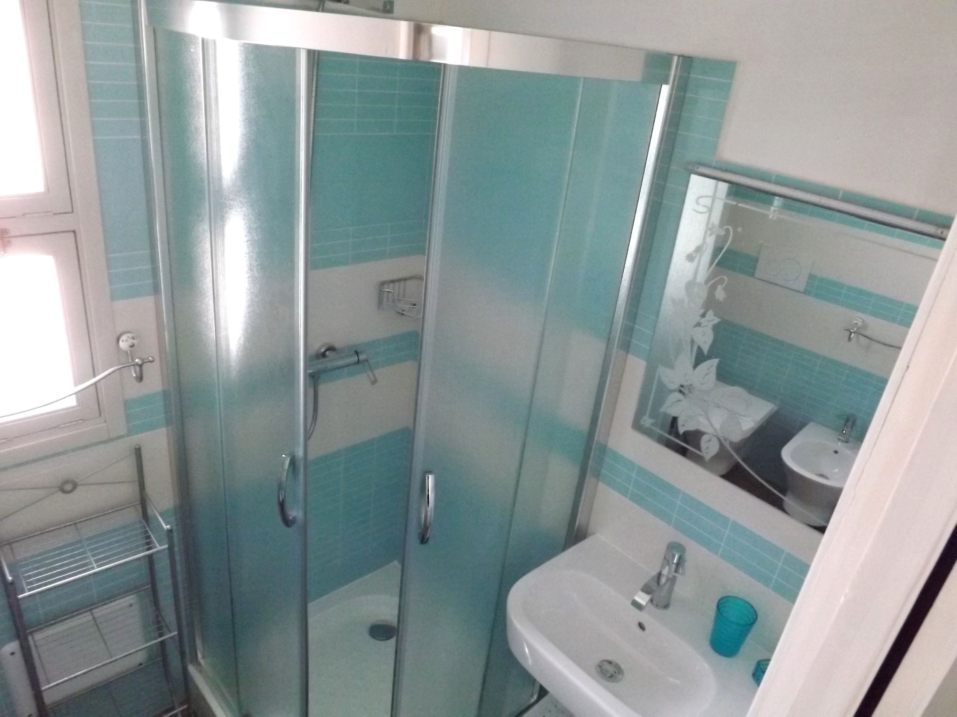 A bathroom with a glass-enclosed shower, a sink, and a mirror.