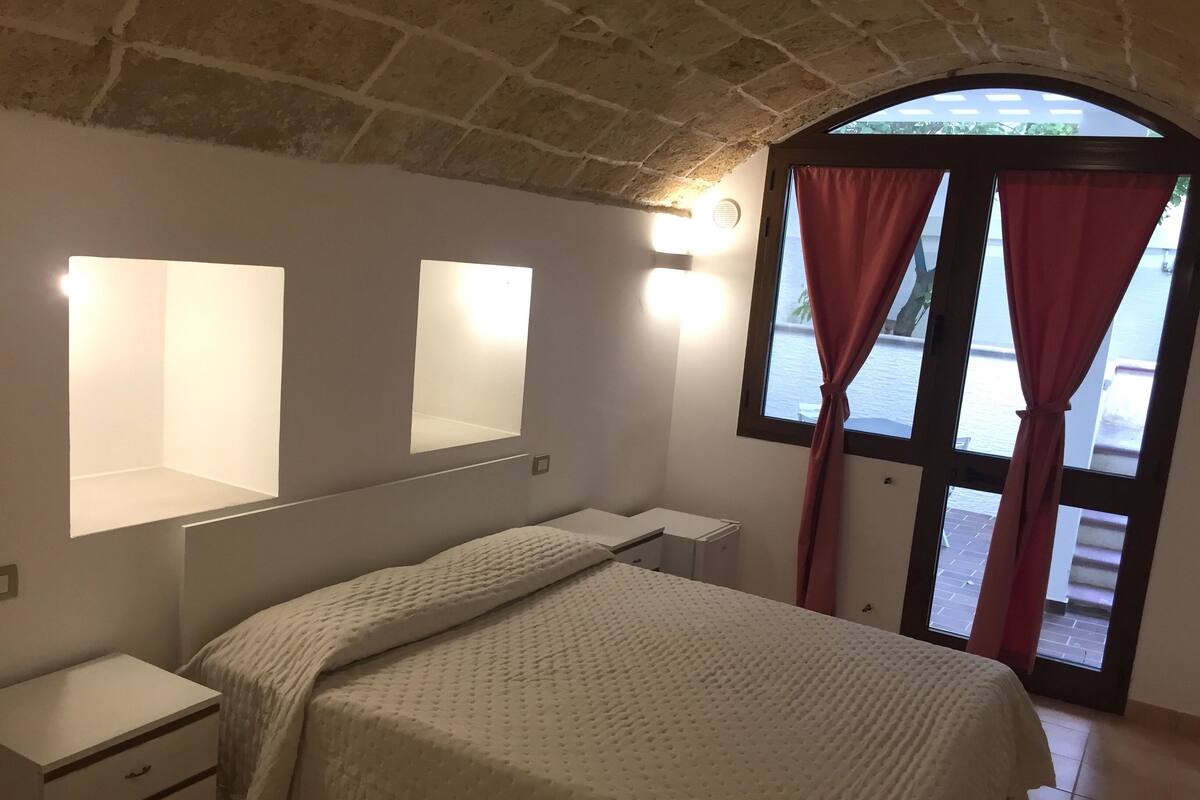 A bedroom with a bed, bedside tables, a mirror, and a window with curtains.