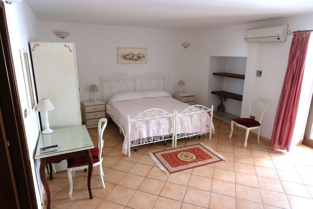 A bedroom with a bed, bedside tables, a desk, a chair, a rug, and a window with curtains.