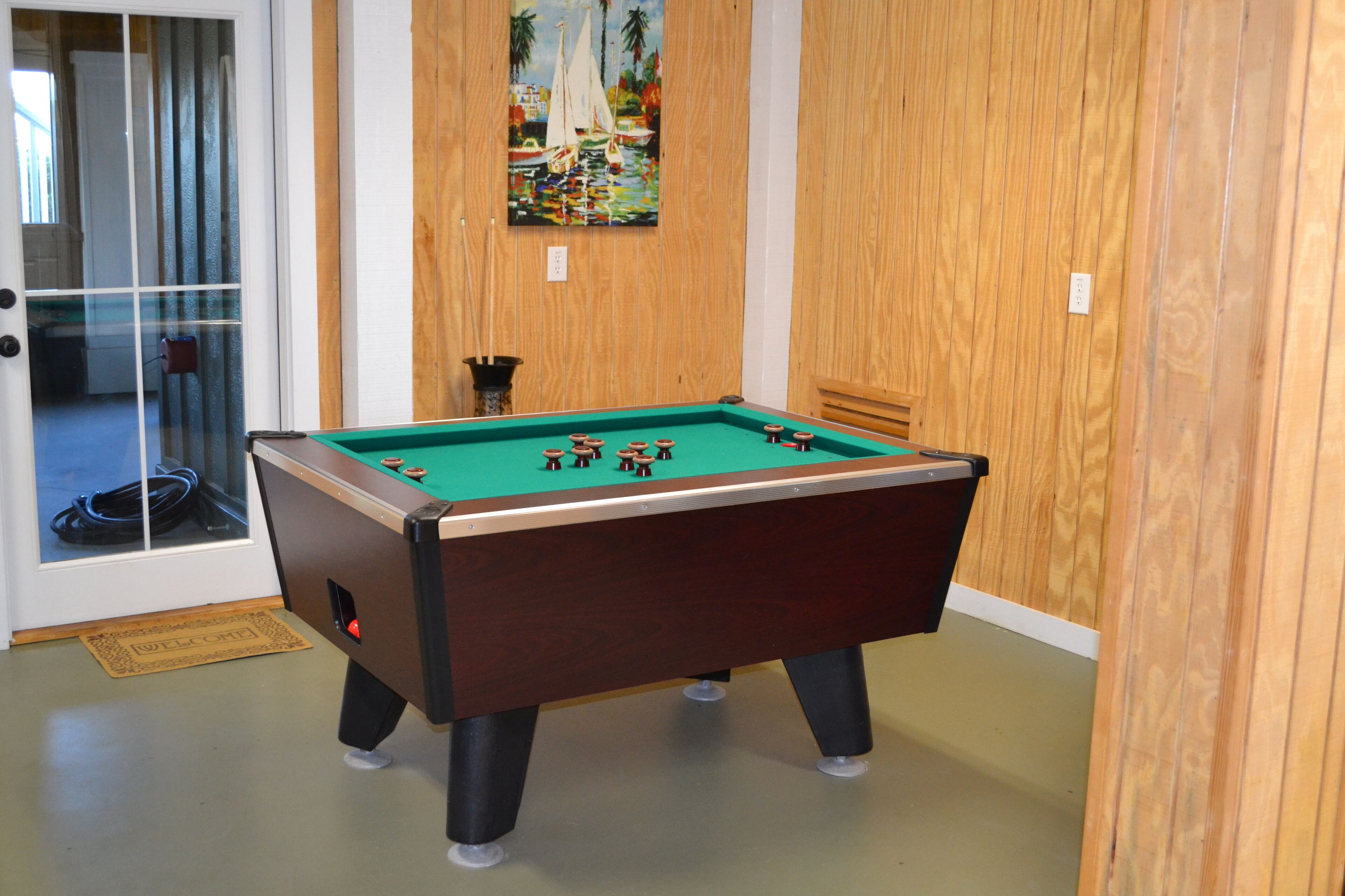 Une table de billard dans une pièce aux murs lambrés, avec un tableau représentant des voiliers accroché au mur.