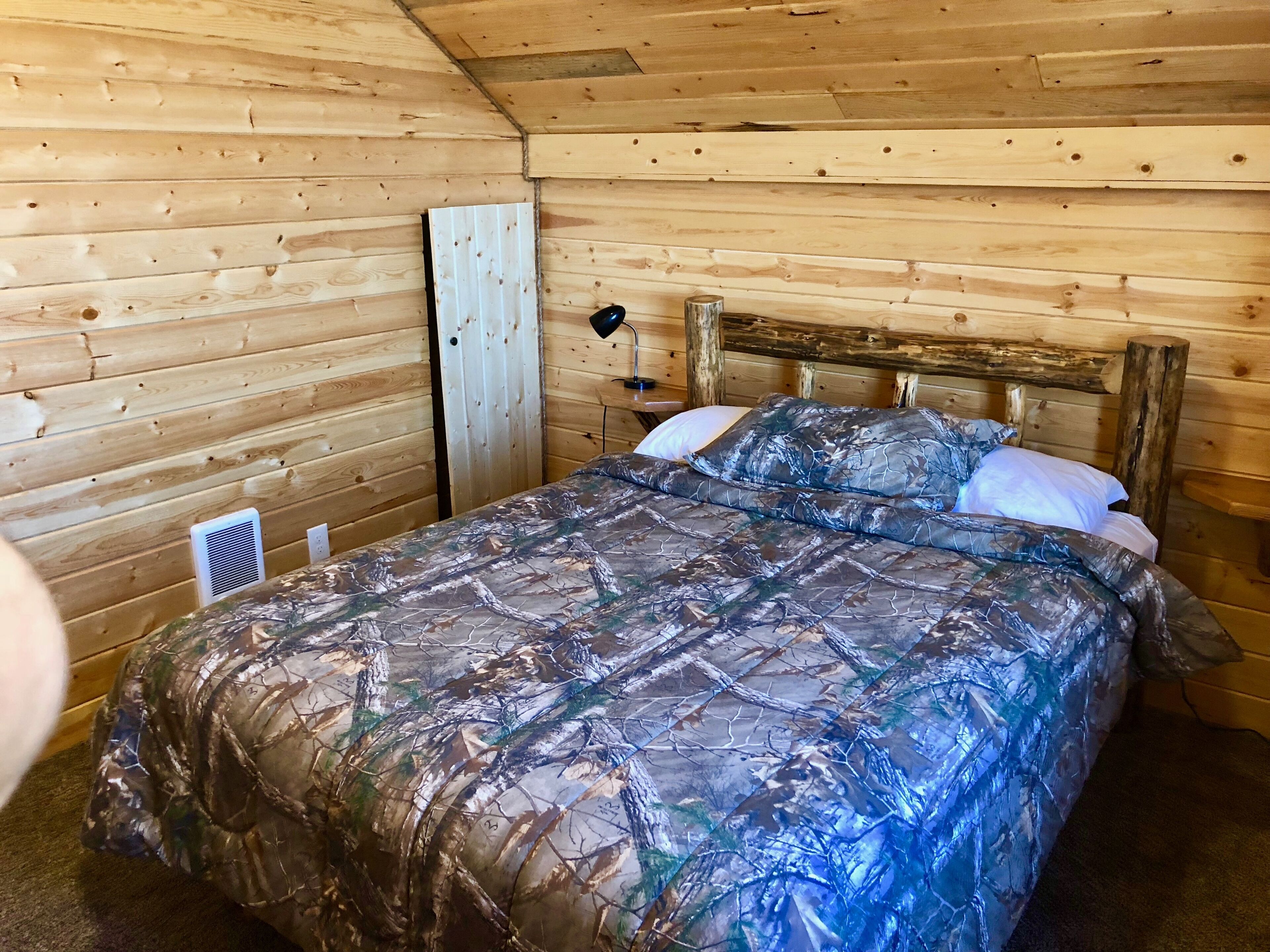 Ein Schlafzimmer einer Holzhütte mit einem Bett, einem Nachttisch und einer Wandleuchte.
