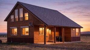 Une cabane en bois à deux étages, dotée d’un toit en pente, de grandes fenêtres et d’une véranda.