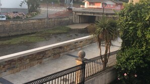 A riverside walkway with a stone wall, a bridge, and residential buildings in the background. - Hotel La Bilbaina (Vegadeo)