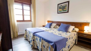 A double bed with floral bedding, a bedside table with a lamp, and a window with curtains. - Hotel La Bilbaina (Vegadeo)