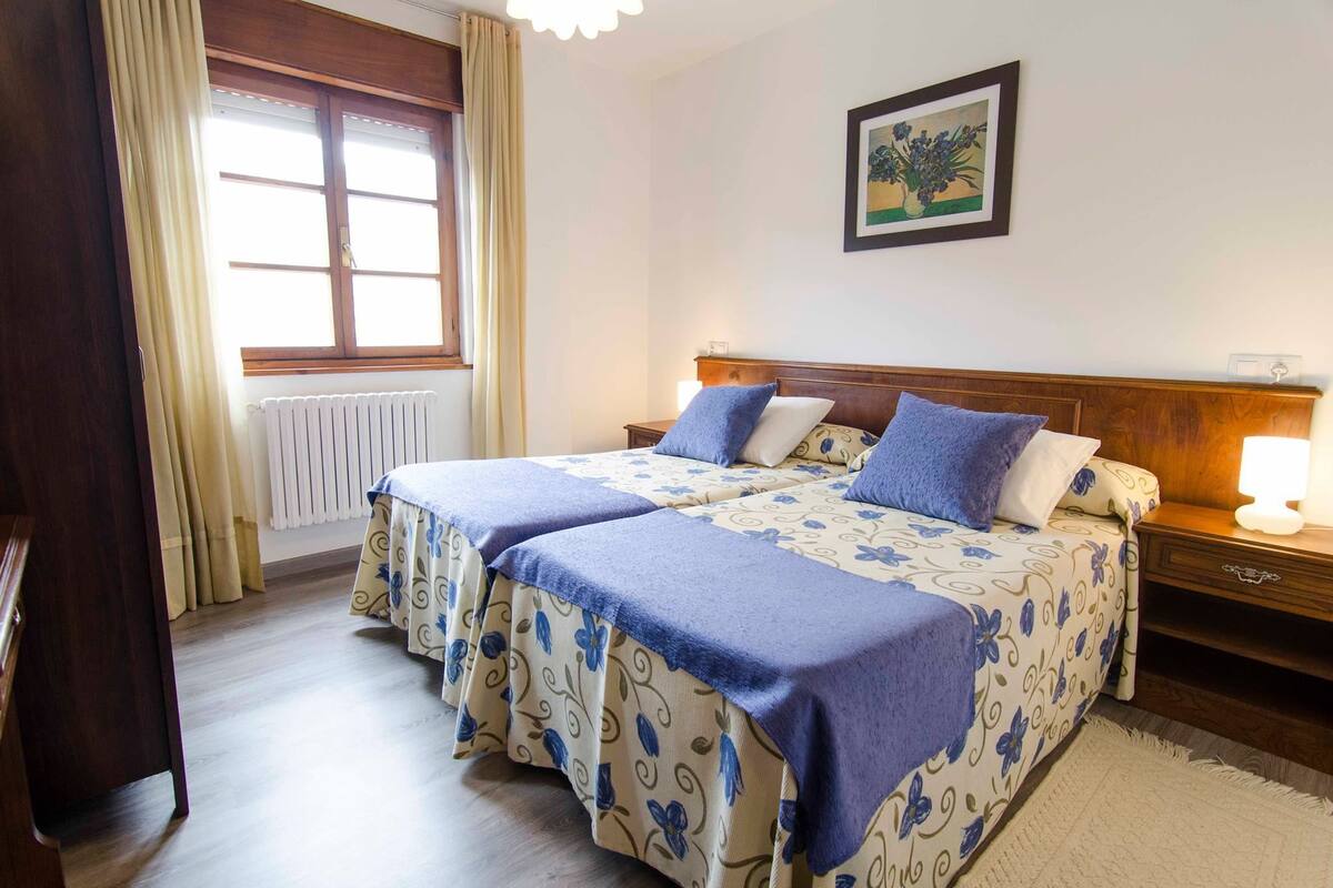 A double bed with floral bedding, a bedside table with a lamp, and a window with curtains.