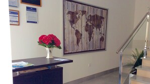 A reception desk with a vase of flowers, a world map on the wall, and a staircase with glass railings. - Hotel La Bilbaina (Vegadeo)