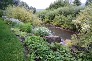 A garden with a stream, lush greenery, and a rock formation.