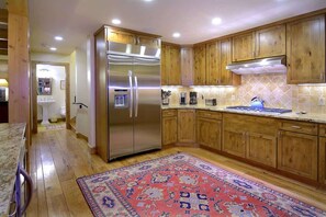 A kitchen with wooden cabinets, a stainless steel refrigerator, a tiled backsplash, and a patterned rug.