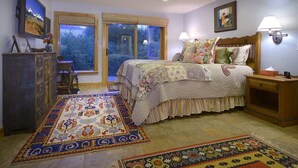 A bedroom with a bed, a nightstand, a dresser, a television, and a window with a view of trees.